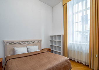 View of bed and window with curtain in bedroom interior. White walls.