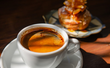 Black coffee and orange bread placed on a wooden table on a sunny day.