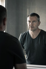 Man in grey v-neck tshirt staring at himself in bathroom mirror