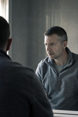 Man in grey polar fleece staring at himself in bathroom mirror