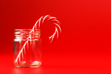 Lollipop Candy cane in a glass jar on a red background.