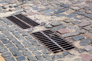 the 2 iron grates of the drainage system hatch on the road paved with paving stones, closeup of a sewer grates.