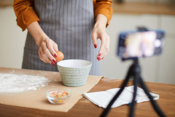 Cropped portrait of unrecognizable young woman breaking eggs while filming baking tutorial for video channel, copy space - obrazy, fototapety, plakaty