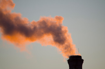 Bright colored smoke from the factory pipe, illuminated by the setting sun. Close-up.