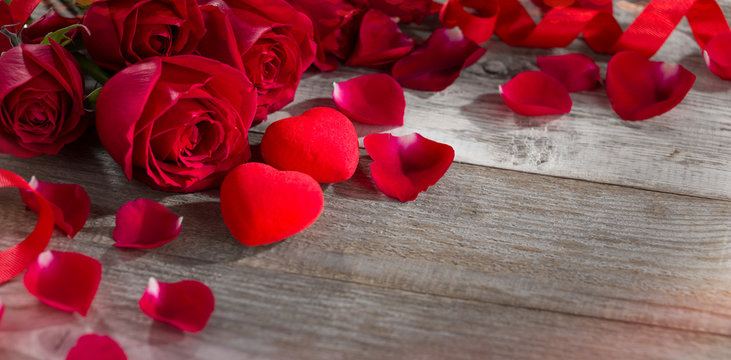 Red hearts with roses and rose petals on old wooden table