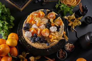 Homemade cake decorated with clementines, kumquat and fresh berries on dark background