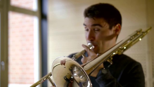 professional musician is playing by trombone indoors, medium shot