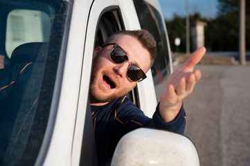 Young man with sunglasses comes out of the car window with his head with his arm raised. Face...