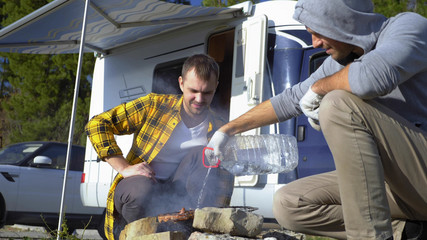 Two men cook meat on the grill near the campervans in nature
