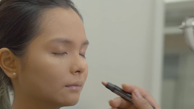 Young, attractive Asian model getting makeup put on py a professional artist in a photography studio