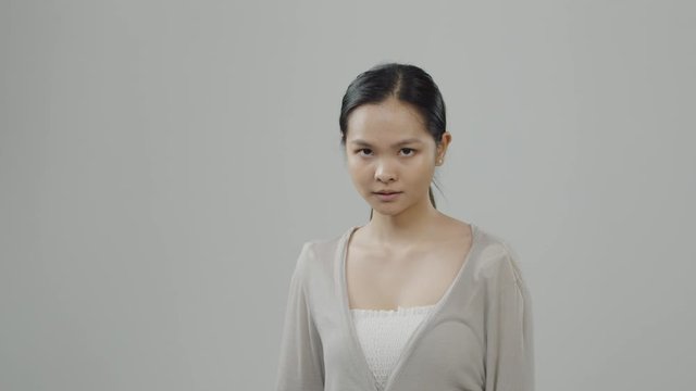 Young, attractive Asian woman with long hair pulled back in a ponytail poses with a strong expression for a casting audition - beige sweater over white shirt against white background