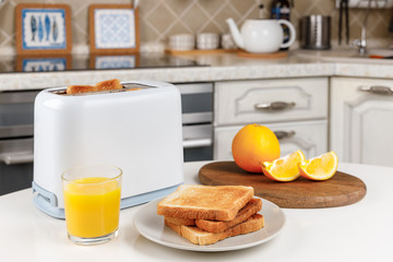 White toaster, glass of orange juice, crispy toasted bread on the plate and fresh oranges on wooden board. Looking yummy for morning meal. Kitchen interior. Fresh delicious breakfast concept.