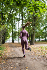 Obraz premium Young woman runner running during outdoor workout in the park. rear view