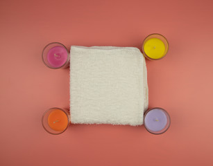 White towel and scented candles on a pink background, top view. Spa concept.