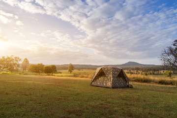 Camping tent on green field near forest during dramatic sunrise at summer misty morning,Concept of outdoor camping adventure