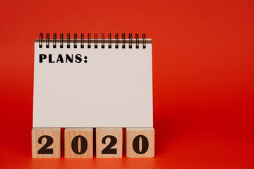 2020 new years goals plans and resolution concept, book with blank page with lots of copy space and wooden blocks with the year 2020 written on red background