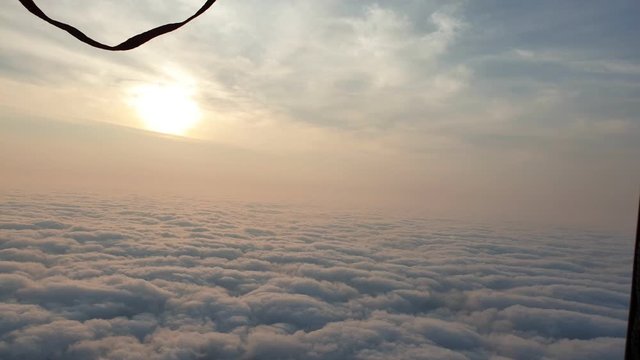 Adventure first person view, pov from basket of field, meadow, river and above cloud in flight on hot air balloon. The aircraft fly in morning blue sky. Hot air balloon burner flame into envelope.