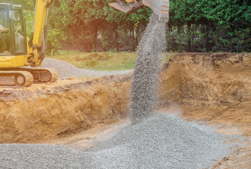 Excavator digging bucket scooping gravel from a building foundation