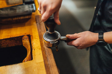 Barista grinding coffee in portafilter in coffee shop.