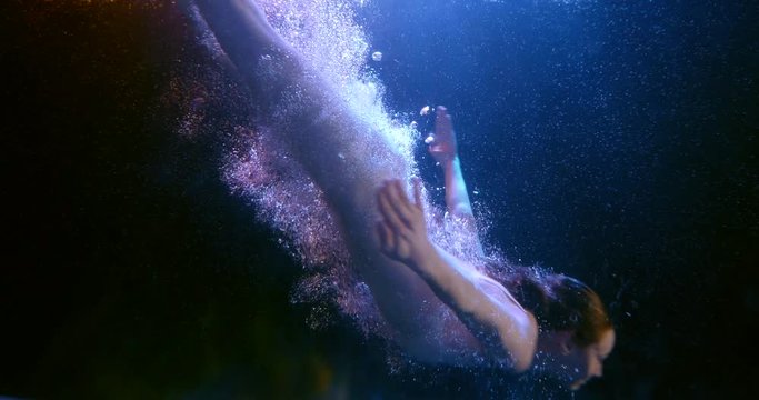 Slender girl diving under water in the dark. Diving to the depths in slow motion