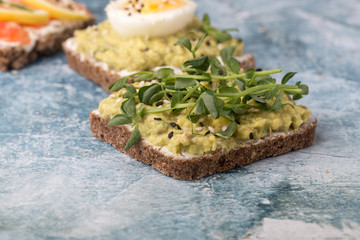 Open sandwiches with avocado, micro greenery on a blue stone background. Close-up