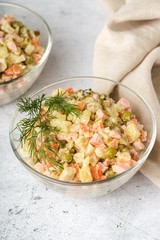 Russian traditional salad Olivier with boiled vegetables, in a glass salad bowl on the table. Gray background.