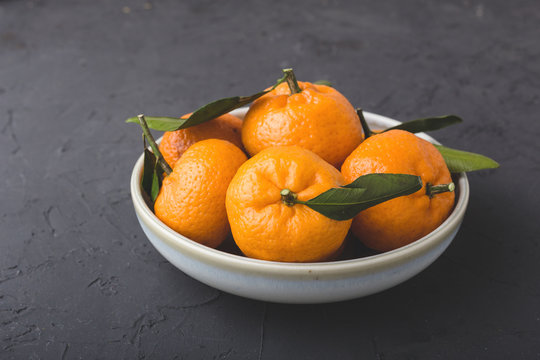 Tangerines with leaves in a dish on a dack background. Close-up