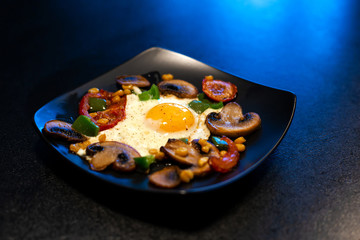 Freshly fried scrambled eggs with vegetables on a black plate