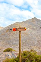 Wooden tourist sign giving direction in Ponta de Sao Lourenco, Madeira, Portugal. Hiking path leading on the cliffs. Hilly terrain. TRANSLATION: Cais do Sardinha - Sardine Pier. Vertical photo