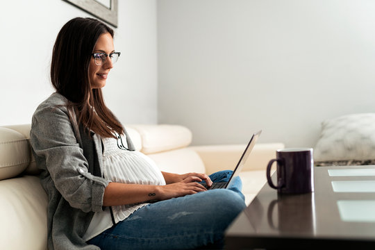 Pregnant woman sitting on couch at home while using the laptop