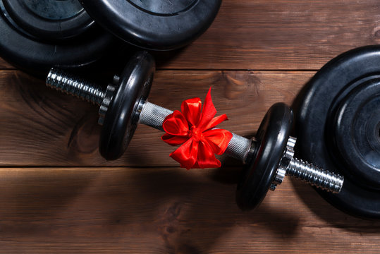 gift - dumbbells tied with a red ribbon on a dark wooden table along with sports equipment