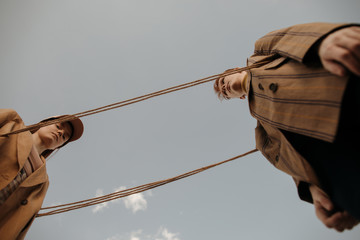 Twins playing with rope against gray sky in countryside