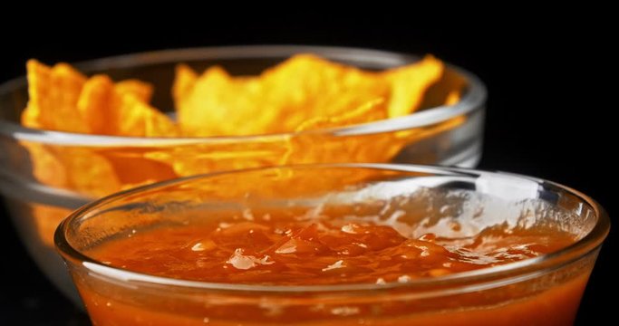 Hand dips tortilla chip into salsa sauce on black background close-up