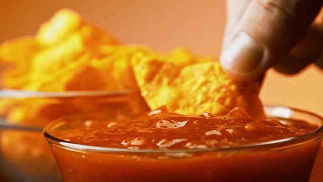 Hand dips tortilla chip into salsa sauce slow motion close-up