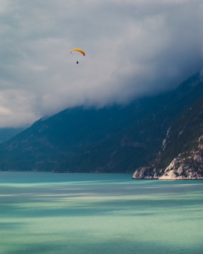 A paraglider flying over glacial water on a foggy day in the mountains