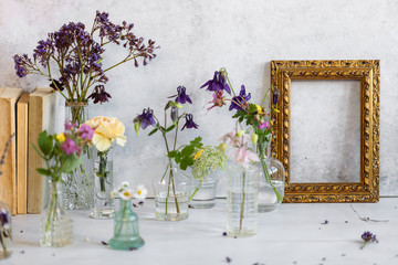 Old books cllse to a collection of glass vases with water and flowers and a golden framing