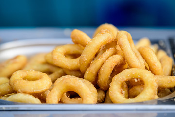 Large group of freshly fried calamari and onion rings on display for sale at a street food festival, ready to eat seafood 