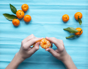 The peeling process of mandarin on blue background.  Hands of boy clean tangerine,  top view. 