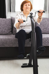 Fototapeta na wymiar Senior woman training at home. Senior woman make exercise at home on a bicycle to maintain joints in the hands and feet