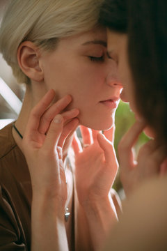 tender portrait of two lesbian faces close in warm light, stroking each other's faces