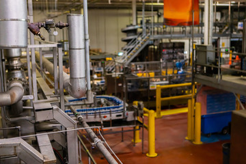 piping systems, industrial valves and metal pipes selective focus against belt conveyor system and other machines in brewhouse brewery beer factory