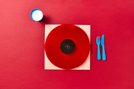 Red vinyl record with plastic disposable houseware and milk glass on a red background.