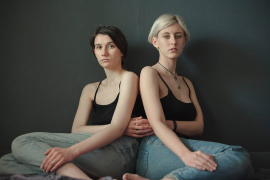 brunette and blonde lesbians sit equally on a neutral background and look at the camera