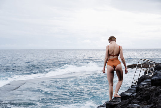 Young female standing near sea and preparing swimming