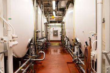 Fototapeta na wymiar passageway between serving vessels, beer pressure lagering bright white tanks, brewing process piping room, modern brewhouse brewery factory machinery