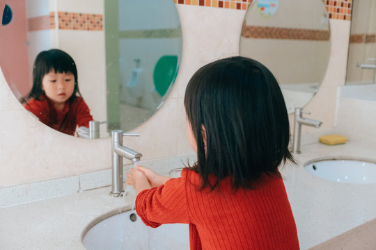 Reflection of girl in mirror while washing hands in sink