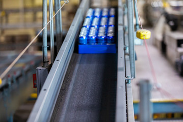 beer aluminum cans on belt conveyor system selective focus and close up view, modern brewhouse brewery factory packaging industrial machines