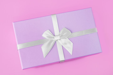 Gift box with a white silver bow, lilac on a pink background. Holiday gift minimal concept. Top view, flat lay, close-up.