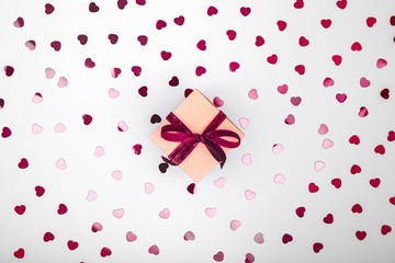 Craft box with dark red velvet ribbon bow and glitter heart confetti. Valentine day and eco-friendly wrapping concept. Trendy minimalistic flat lay design background. Horizontal