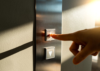a woman's finger presses the Elevator button in the sunlight